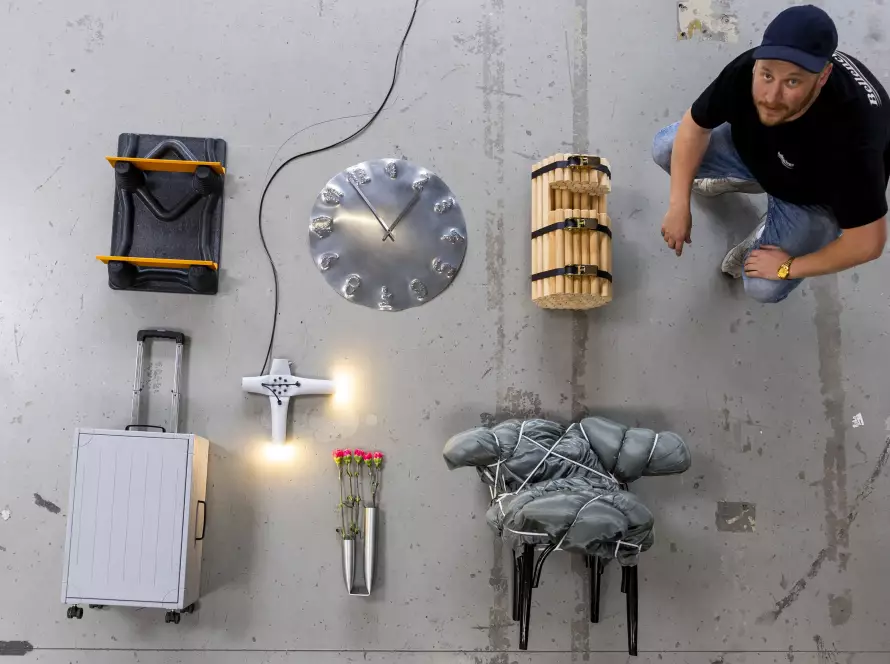 Der Wiener Künstler Thomas Waidhofer sitzt auf grauem Boden neben mehreren seiner Objekte während der Ausstellung im MANANA cafẽ, fotografiert von Martin Steiger.