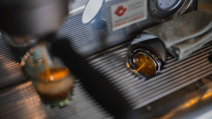 Close-up eines bodenlosen Siebträgers im Spiegel unter der Kaffeemaschine während der Espresso-Extraktion; Fokus auf Espresso zubereiten und Dial-In.