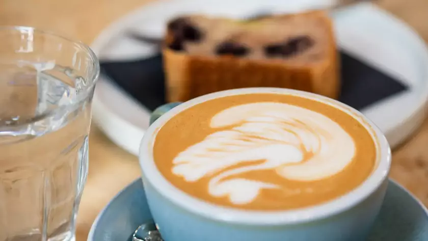 Cappuccino mit Latte Art und Banana Bread auf Tisch im MANANA Café Wien