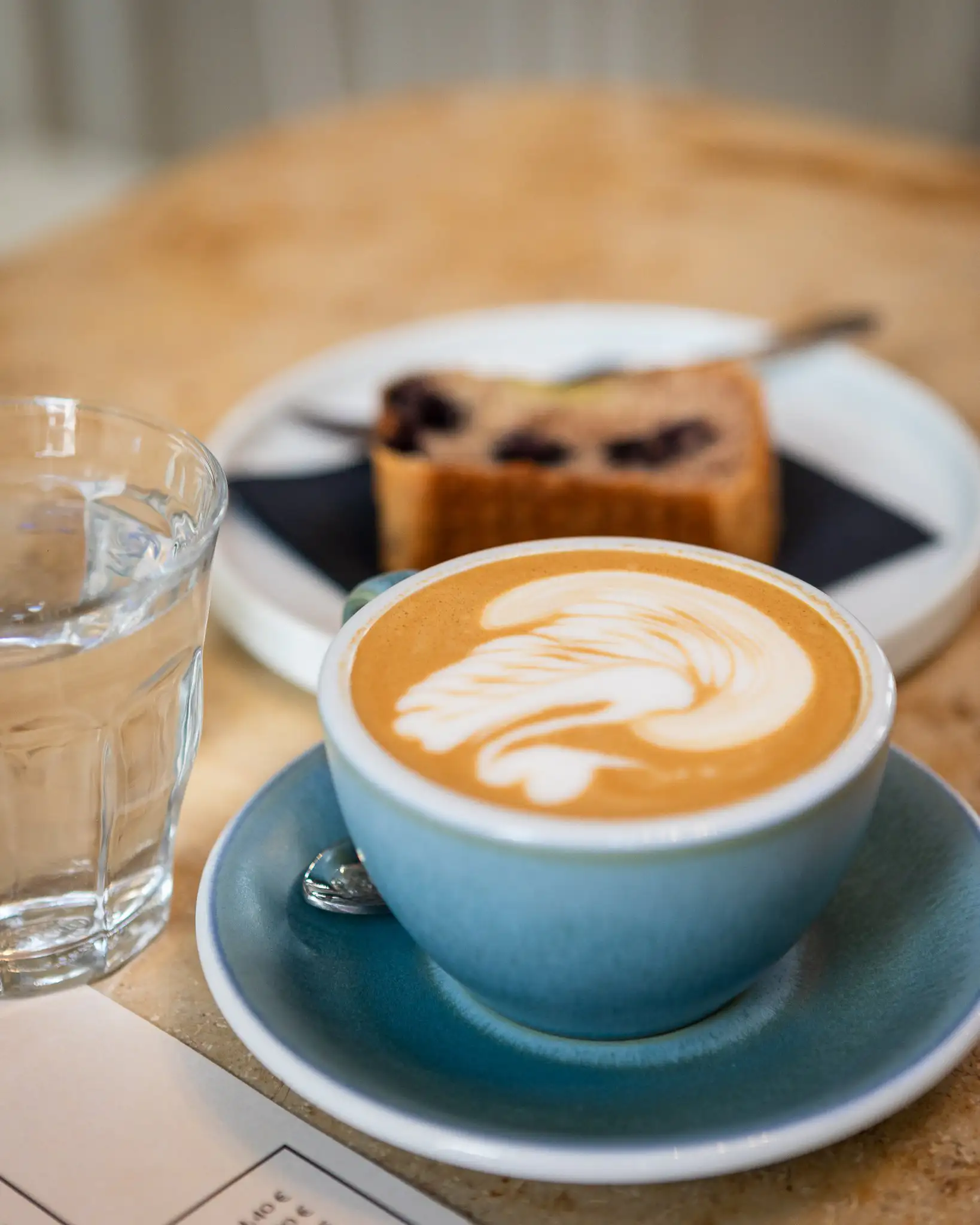 Cappuccino mit Latte Art und Banana Bread auf Tisch im MANANA Café Wien